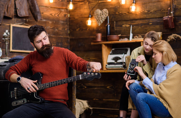 Rock musician with trendy beard and mustache playing guitar. Bearded man tuning musical instrument. Mom and daughter adjusting old video camera while dad is composing music, leisure activity concept - Foto, afbeelding