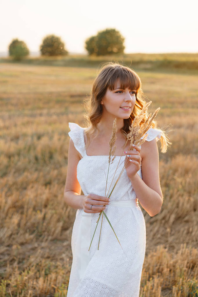 Girl in white dress with spikelets. Woman in field, place for text. Spike and girl in field. Late summer and early autumn. August or September - Фото, зображення