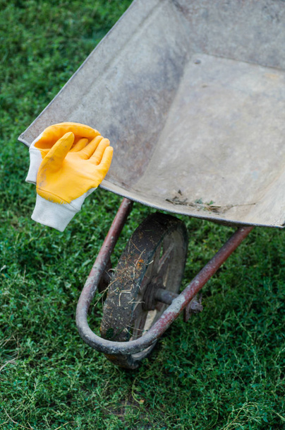 Garden tools, wheelbarrow and yellow gloves. gardening tools. Works outdoors in spring and spring yard cleaning concept. - Photo, Image
