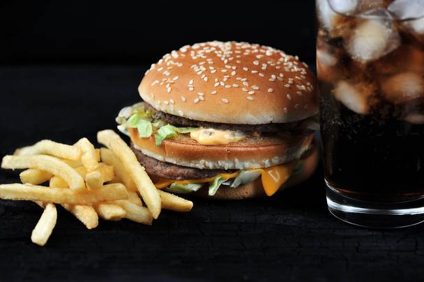 burger with french fries and a glass with ice cola on a black rustic background - 写真・画像