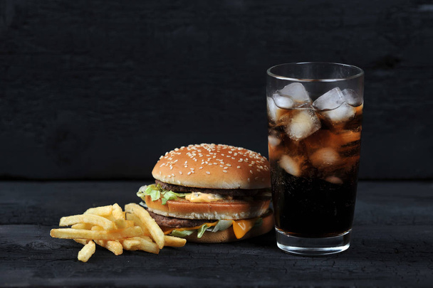 burger with french fries and a glass with ice cola on a black rustic background - Fotó, kép