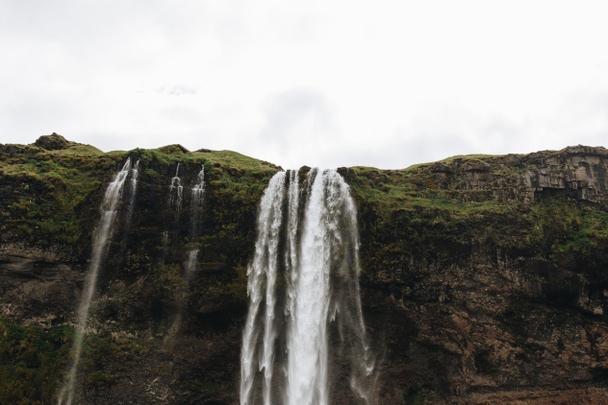 низкий угол обзора водопада Seljalandsfoss в горных районах Исландии
  - Фото, изображение