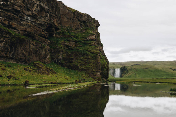 scenic view of beautiful waterfall Skogafoss in highlands under cloudy sky in Iceland  - Photo, Image
