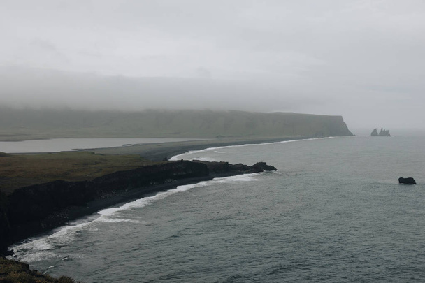 aerial view of rocky cliff and black sand beach under cloudy sky at Dyrholaey promontory in Vik, Iceland - Photo, Image