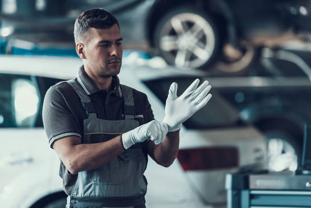 Auto Mechanic Wearing White Gloves in Garage. Portrait of Handsome Serious Caucasian Repairman in Grey Uniform Standing in Front of Car. Repair Service Concept. Automobile Master Concept - Foto, immagini