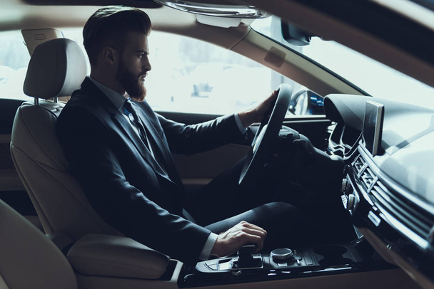 Business Man Driving Car Shifting Gear Stick. Stylish Confident Caucasian Person Wearing Black Suit Posing in Auto with Serious Expression. Driving Automobile with Automatic Gears Concept - Fotografie, Obrázek