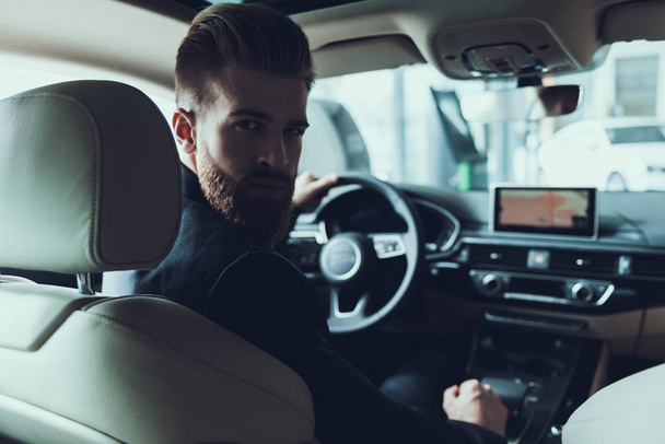 Handsome Bearded Car Driver Looking at Camera. Portrait of Stylish Confident Caucasian Person Posing in Auto Wearing Black Suit Turning to Back Seats with Serious Expression - Foto, imagen