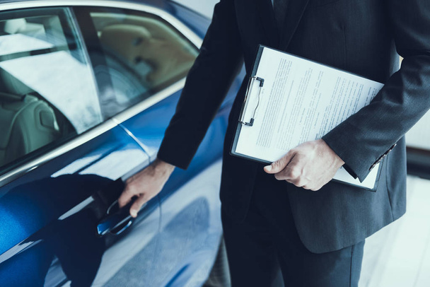 Close-up Of Male Hand Opening Blue Cars Door. Auto Salesman in Black Elegant Suit Holding Clipboard and Standing Close to Cars Door. Auto Buisiness Concept. Automobile consultant - Фото, зображення