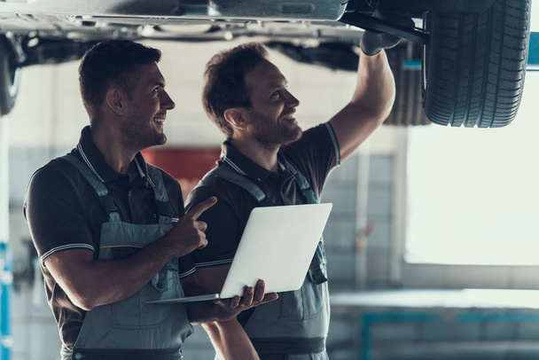 Mechanics Checking Wheel Bearings in Car Workshop. Two Caucasian Adult Technician Master in Uniform Repairing Car. Repairman Looking at Car Using Laptop. Auto Service Concept - Foto, afbeelding