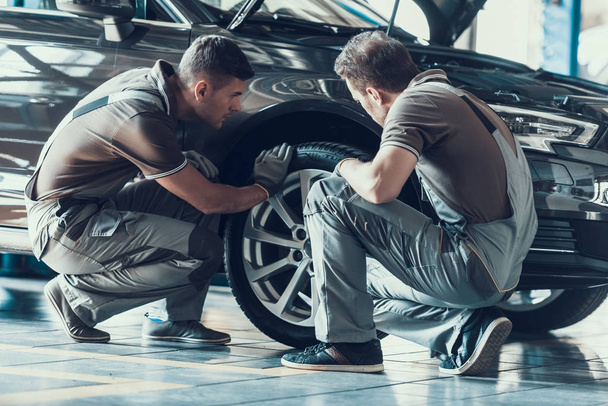 Mechanics Checking Wheel Bearings in Car Workshop. Two Professional Caucasian Adult Technician Master in Uniform in Front of Automobile in Garage. Repairing Car Service Concept - Φωτογραφία, εικόνα