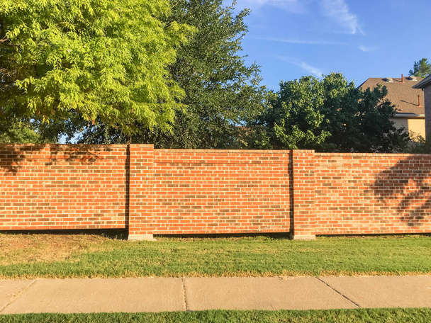 Muros de la subdivisión de ladrillo rojo en Irving, Texas, EE.UU., barrera entre las casas residenciales del barrio y la calle concurrida de derecho de paso público con camino. Pantalla, sonido, muros de dirección y sistema de cercas
 - Foto, Imagen