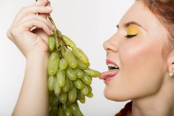 Beautiful redhead woman licks grapes. concept of healthy eating - Photo, Image