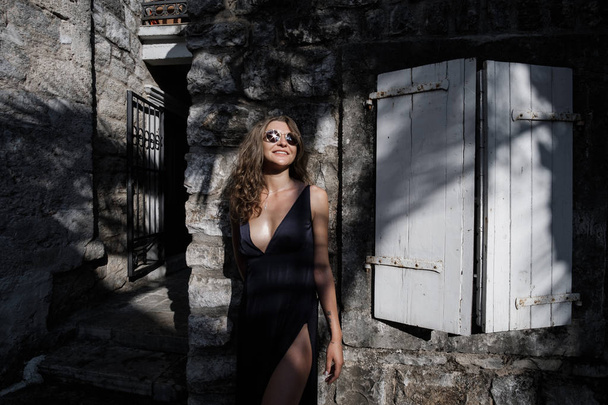 Portrait of Young curly blonde woman in long dress and sunglasses walks around the old town in Budva, Montenegro. Slow motio - Photo, Image