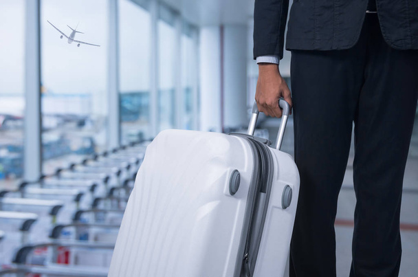 Бизнесмен и чемодан в зале вылета аэропорта, самолет на размытом фоне, концепция летнего отдыха, чемоданы путешественников в зоне ожидания терминала аэропорта
. . - Фото, изображение