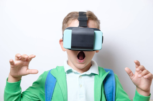 Cute schoolboy with blue backpack wearing virtual reality helmet with arms stretched forward on a white background - Foto, Bild