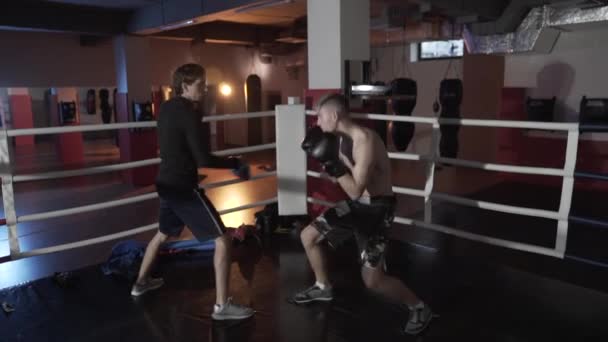 Slow-motion shooting fight club. Boxers train before the fight in the ring. The trainer in boxing paws and a young athlete in gloves practice the technique of combat and dodge attacks. - Video, Çekim