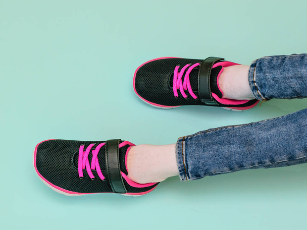 Jambes de fille en jean déchiré et baskets noires et rouges sur fond bleu pastel. Chaussures de sport à la mode. La vue du haut
. - Photo, image