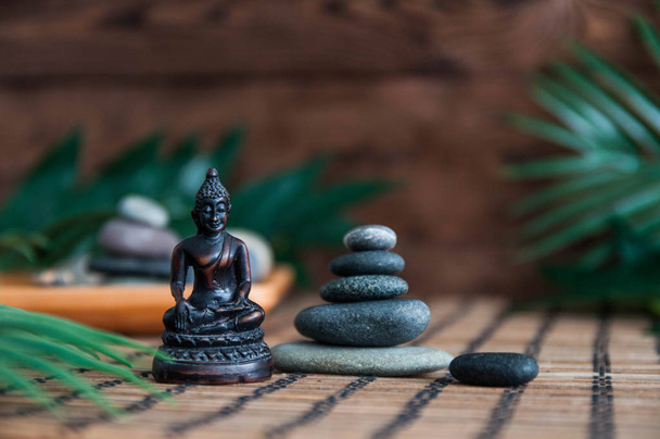 Pyramids of gray zen stones with green leaves and Buddha statue on wooden background. Concept of harmony, balance and meditation, spa, massage, relax - Foto, Bild