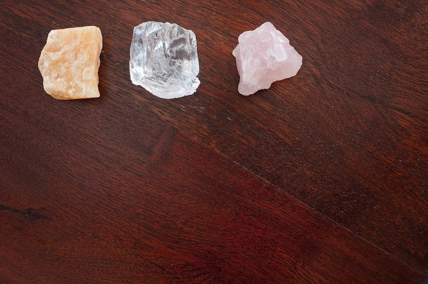 Heilkristalle: Rosenquarz, Calcit und ein klarer Quarz auf einem Tisch. Edelsteine werden für ihre positiven Schwingungen verwendet, um innere Kraft und Frieden und positive Energie in die Meditation zu bringen. - Foto, Bild