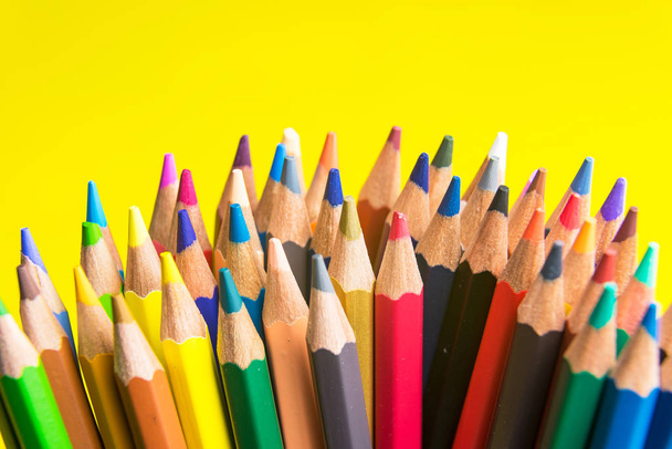 Ensemble de retour à l'école crayons multicolores colorés faisant des formes vue de côté sur un fond jaune - Photo, image