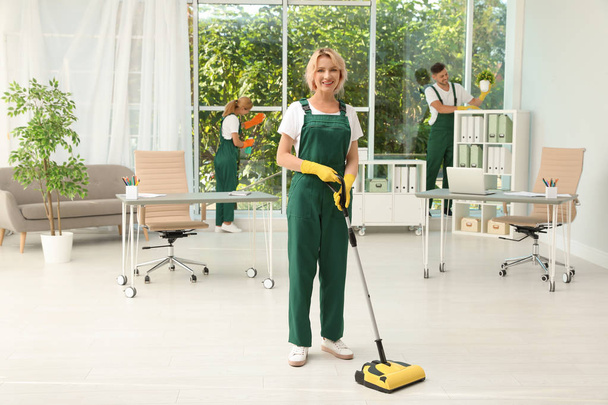 Team of janitors with cleaning supplies in office - Фото, изображение