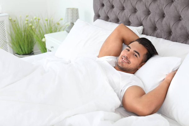 Young man lying in bed with soft pillows at home - Foto, afbeelding
