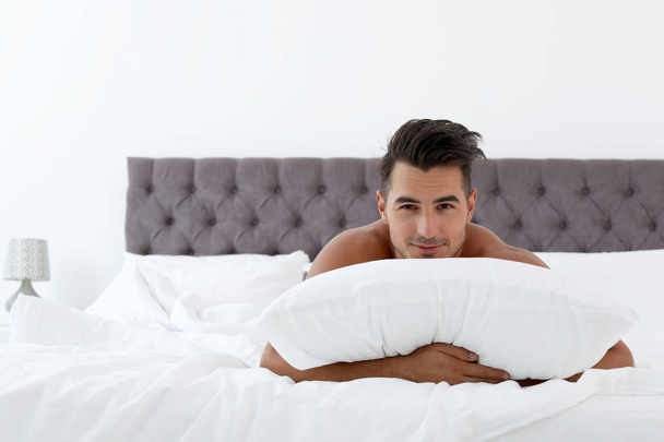 Sexy young man with soft pillow on bed at home - Photo, image