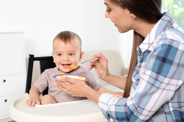 Woman feeding her child in highchair indoors. Healthy baby food - Zdjęcie, obraz