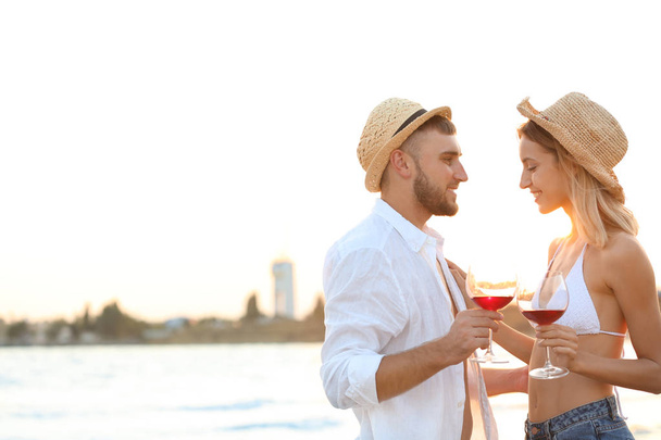 Young couple with glasses of wine on beach - Fotoğraf, Görsel