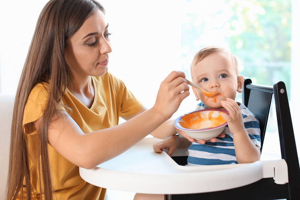 Woman feeding her child on couch indoors. Healthy baby food - Фото, зображення