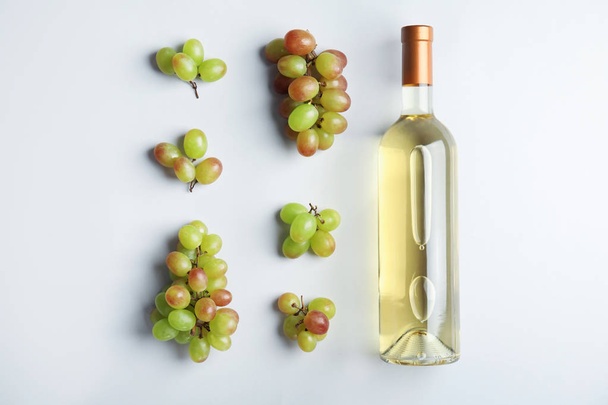 Bottle with white wine and fresh ripe juicy grapes on light background, top view - Foto, Imagem
