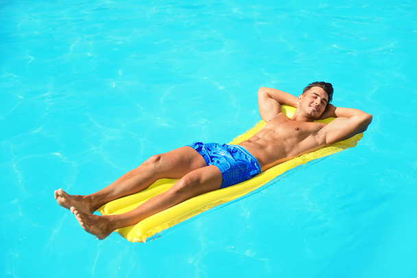 Young man with inflatable mattress in pool on sunny day - Fotó, kép