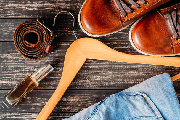 Chaussures décontractées en cuir marron jeans, ceinture et parfum sur fond bois foncé vue de dessus
 - Photo, image