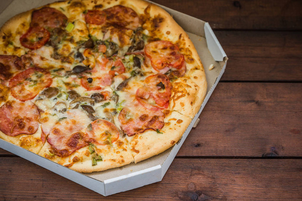 Pizza on wooden background in rustic style. Italian pizza from the shop in a cardboard box. Simple food on a wooden background. Tasty dish for lunch - 写真・画像