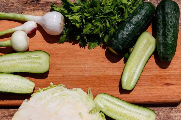 Інгредієнти для весняного овочевого салату на сільському дерев'яному столі. Капуста, огірки, цибуля і петрушка на дошці для різання деревини
 - Фото, зображення