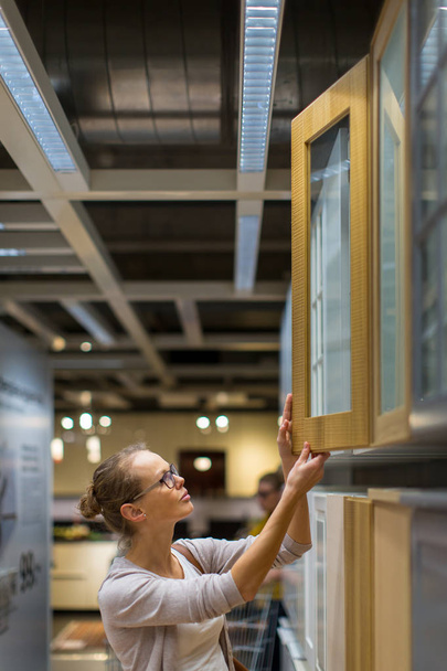 Красивая, молодая женщина выбирает правильную мебель для своей квартиры в современном магазине домашней мебели (цветной тонированный образ; мелкий DOF) - Фото, изображение