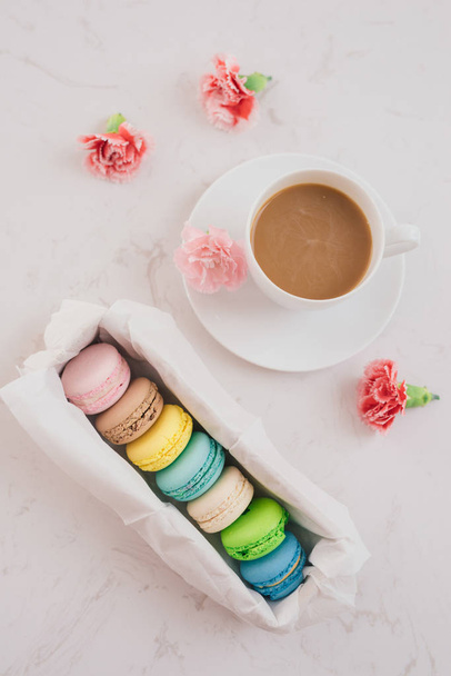 Macarrones de colores franceses en caja de regalo, taza de café y flores en mesa blanca, vista superior
 - Foto, imagen