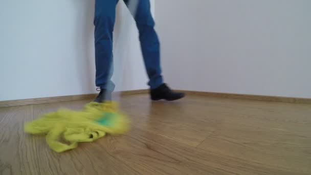 Man wearing blue shoes and trousers, washes the parquet floor with the yellow mop - Záběry, video