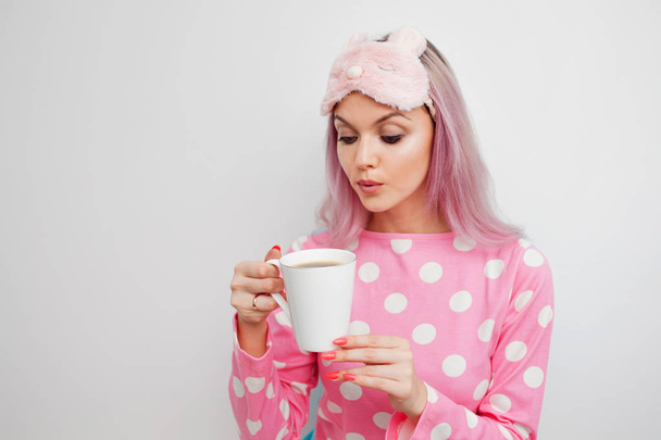 Attractive girl in pink pajamas and sleep mask enjoying her morning coffee - Foto, imagen