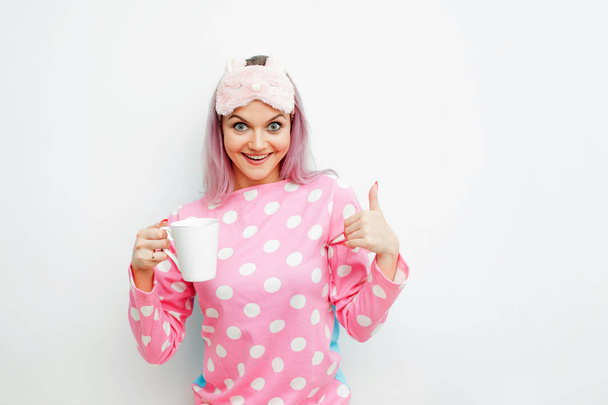Good Morning. Smiling young woman shows thumb up. Girl in pink pajamas and sleep mask - Foto, imagen