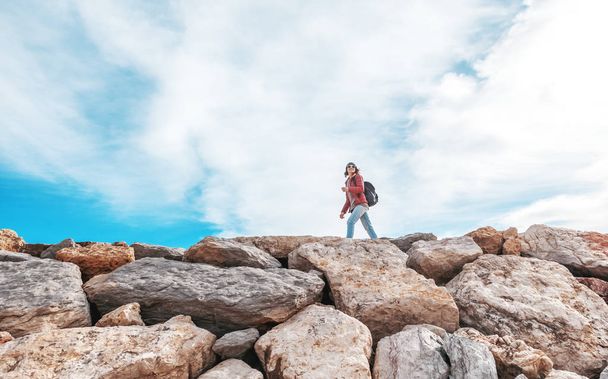 Mooie jonge vrouw reiziger wandelen op rotsen stenen tegen de blauwe hemel in hoed en zonnebril Algarve, Portugal - Foto, afbeelding