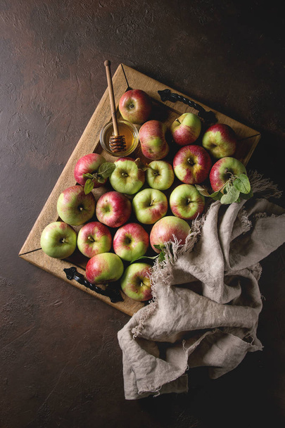 Ripe organic gardening green red apples with leaves and jar of honey on wooden tray and cloth over dark texture background. Flat lay, space. Autumn harvest. - Foto, afbeelding