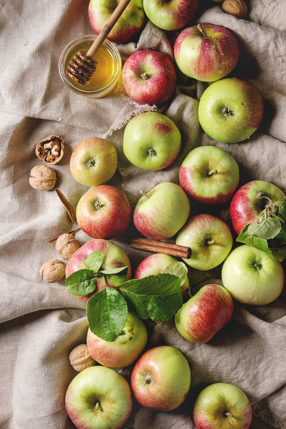 Ripe organic gardening green red apples with leaves, walnuts, cinnamon and jar of honey over linen cloth as background. Flat lay, space. Autumn harvest. - Фото, изображение