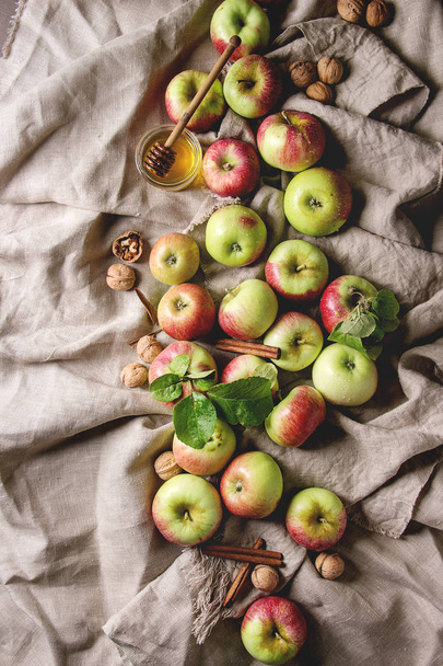 Ripe organic gardening green red apples with leaves, walnuts, cinnamon and jar of honey over linen cloth as background. Flat lay, space. Autumn harvest. - Valokuva, kuva