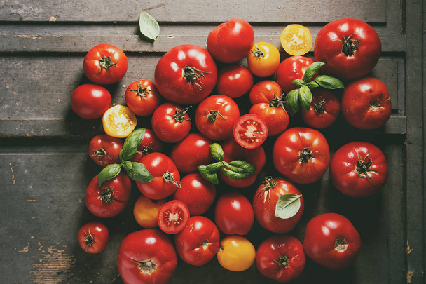 Variety of ripe fresh organic gardening tomatoes different kind and colors with water spot and basil leaves over old grey wooden background. Flat lay, space - Fotoğraf, Görsel