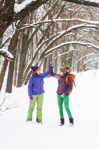 Dziewczęta dają pięciu do siebie. Friends iframe przejdź przez las zima. Kobiety z plecakami spacer przez snow park. - Zdjęcie, obraz