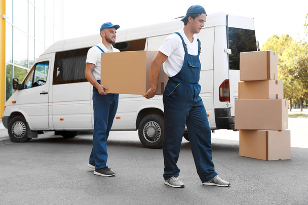 Male movers unloading boxes from van outdoors - 写真・画像