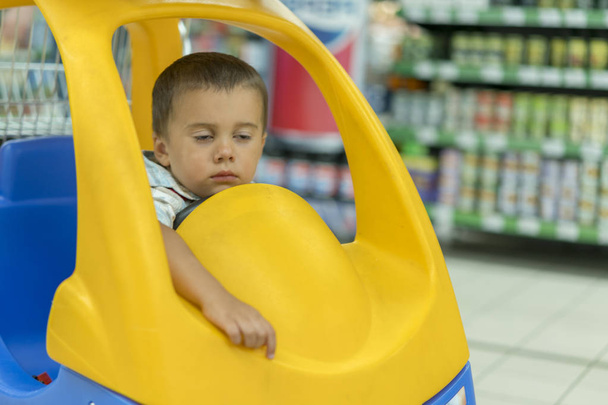Baby schläft in einem Einkaufswagen in einem Supermarkt. schlafender Junge liegt im Stuhl auf dem Einkaufswagen im Supermarkt - Foto, Bild