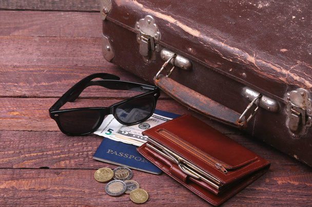 Travel concept with Vintage suitcase, sunglasses, old camera, suede boots, case for money and passport on wooden floor. - Фото, изображение