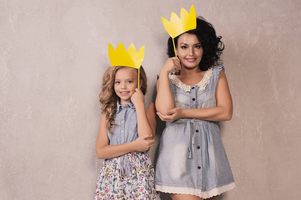 Мать и ее дочь девочка с бумажными аксессуарами. Мама и ребенок держат бумажную корону на палочке
. - Фото, изображение